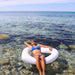 woman in blue swimsuit floating in shallow on white heart pool float, one arm behind her head 