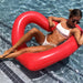 Girl in white swimsuit and sunglasses lounges in the shallow end by stairs in red heart shaped pool float