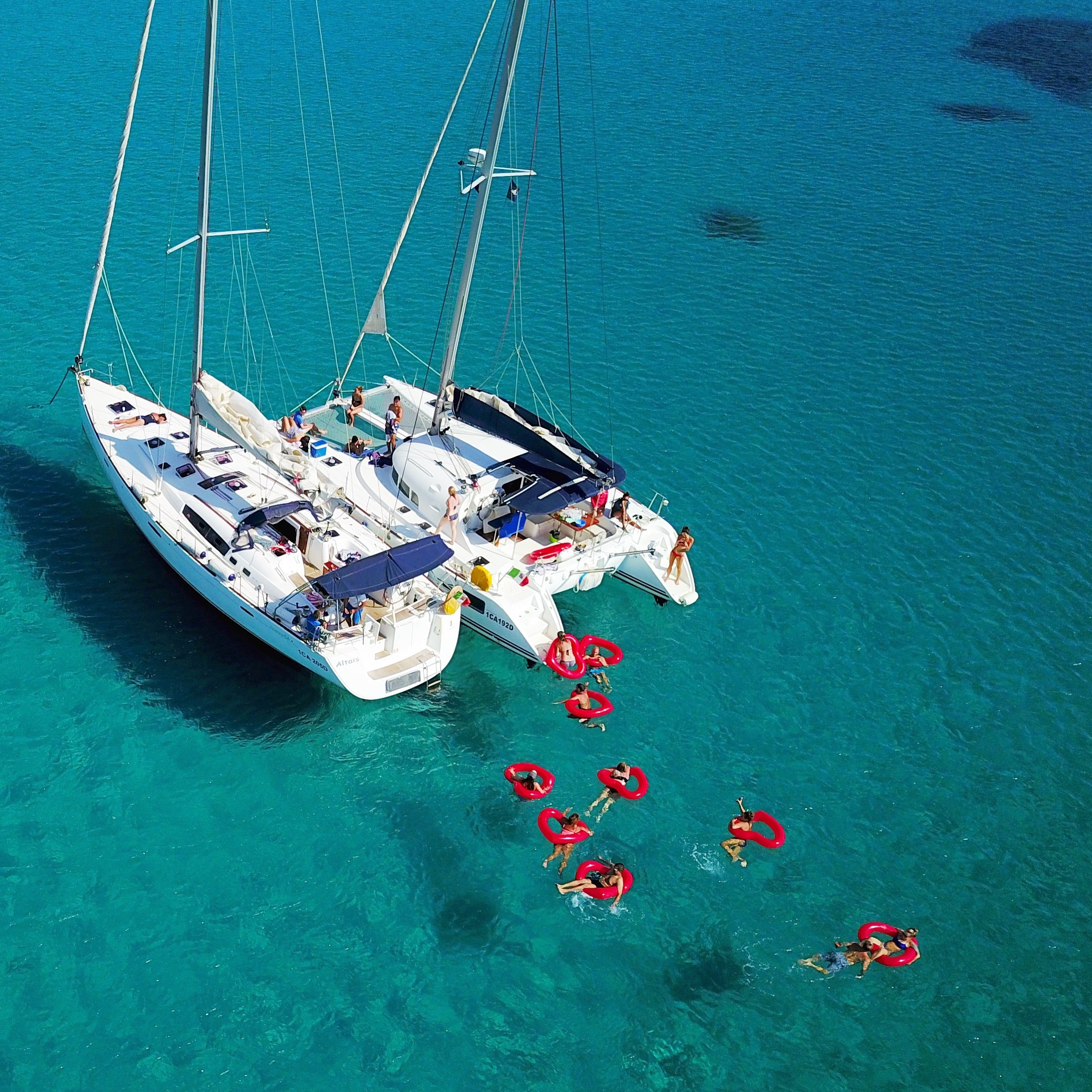Ariel photo of a group of people in the sea, in lôteli red heart shaped floats off two boats in clear blue water