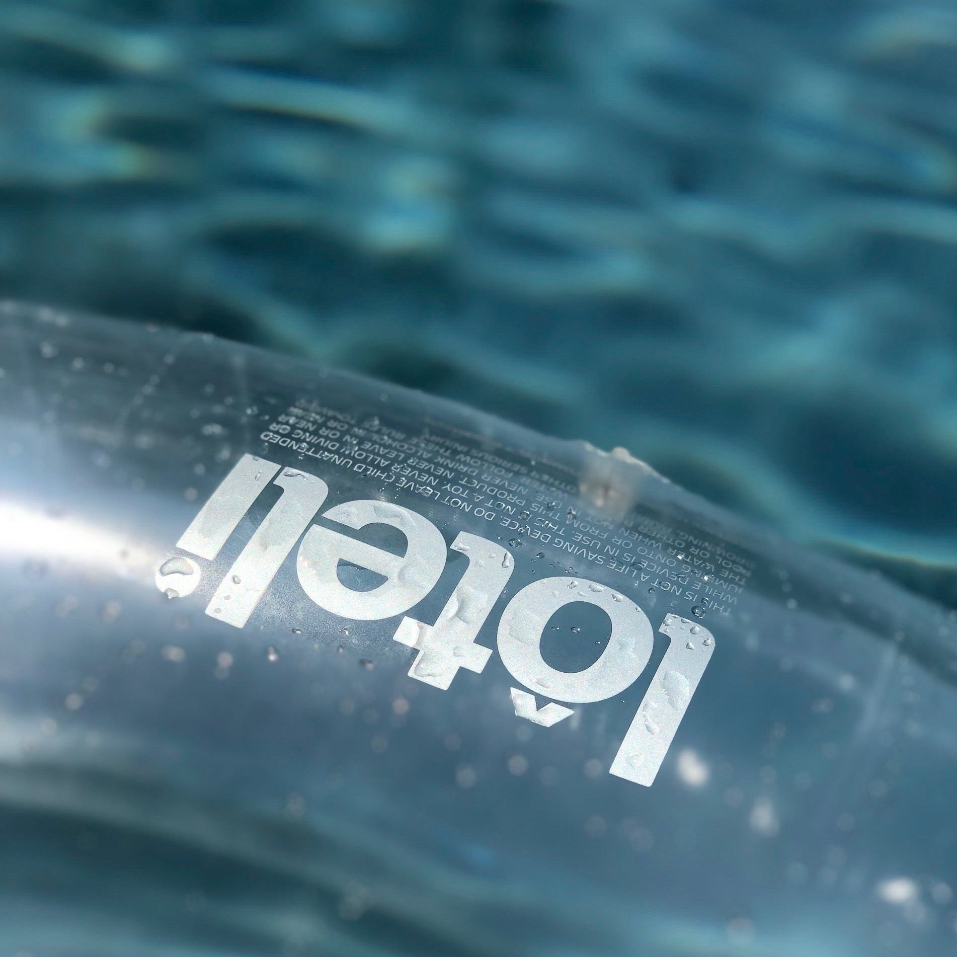 Close up photo of silver loteli logo and double valve on clear ring pool float