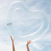 Clear heart float being held up in the air with two pretty feminine hands