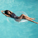 Woman in black swimsuit is relaxing on a clear swim ring from Lôteli, the best pool float brand. Her legs are crossed and her arms stretched above her head